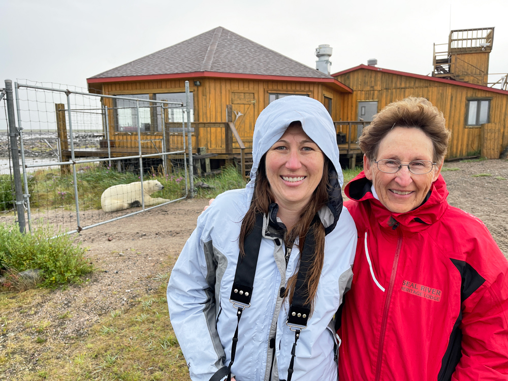 Veterinarian Kathryn Cehrs and her mother Anne at Seal River Heritage Lodge. Polar bear in the background. Birds, Bears & Belugas. July 2023.